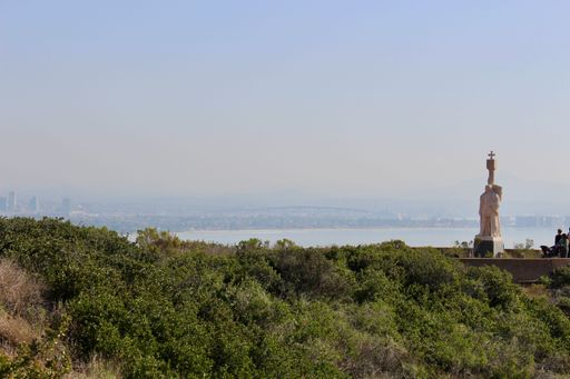 A scenic view from Cabrillo National Monument overlooking San Diego Bay with a statue and city skyline in the distance.