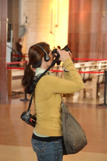 A woman in casual clothing photographs the interior with a camera while wearing headphones.
