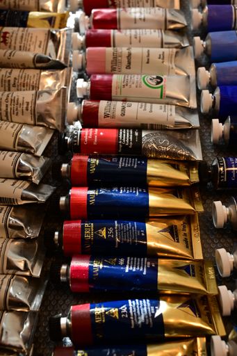Assorted colorful oil paint tubes on a textured surface, showcasing various hues and brands.