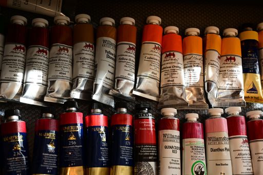 Assorted colorful oil paint tubes in a drawer, displaying various hues and brands on a textured surface.