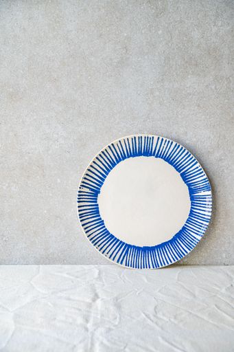 A decorative ceramic plate with blue stripes against a textured concrete background