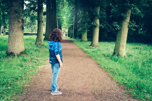 A young girl wearing casual clothes is standing and looking on a walkway in the park