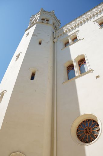 Low angle view of a historic white castle tower with ornate windows against a clear blue sky.