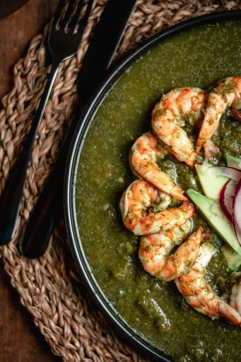 A top view in a vertical format of a tasty shrimp with sauce in a black plate, knife and fork