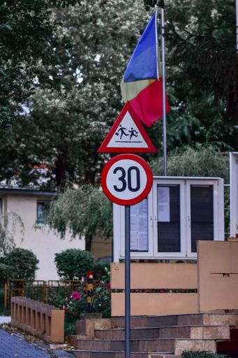 A vertical shot of the Romanian flag and a traffic sign about the speed limit
