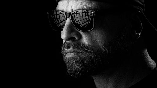 A portrait of a male with a beard and sunglasses isolated on black background