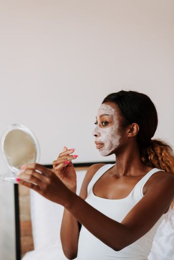 A young beautiful black female holding a mirror applying the mask on her face