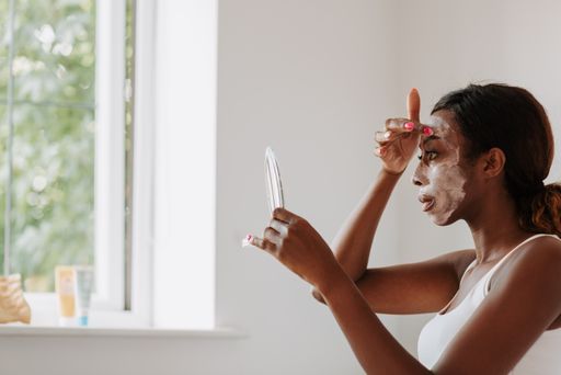 A young beautiful black female holding a mirror applying the mask on her face