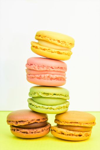 A vertical shot of colorful macaroon biscuits on a green surface with white background