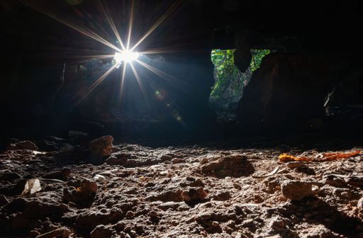 Sunlight beams through a cave entrance illuminating the rocky ground, creating a dramatic and serene atmosphere.