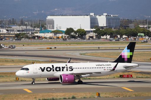 A close-up of a Volaris Airbus A320 taxiing on the runway with clear markings and cityscape behind.