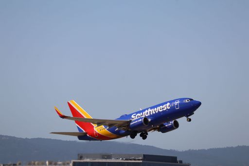 A Southwest Airlines plane is captured mid-takeoff against a mountainous backdrop and urban skyline.