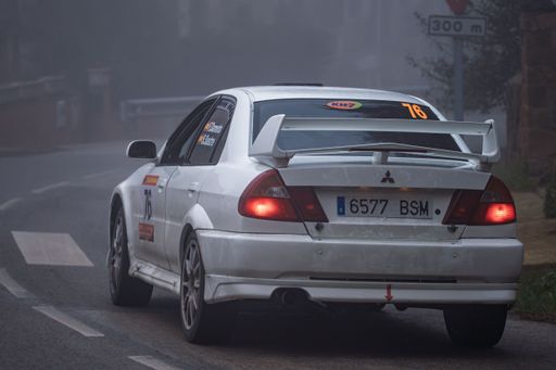A white Mitsubishi Carisma GT Evo VI rally car navigates a foggy road, showcasing its performance and design in a dynamic motorsport setting.