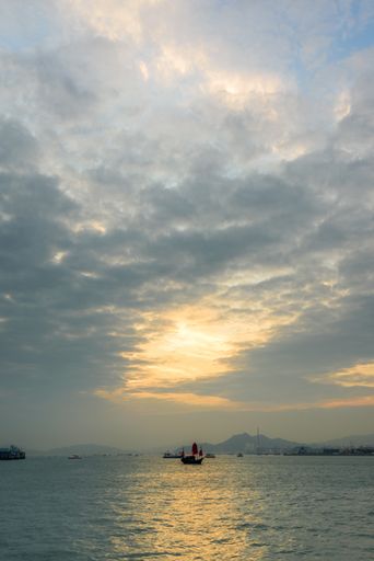 A vertical low angle shot of the boats on the water under the beautiful cloudy sky in Hong Kong