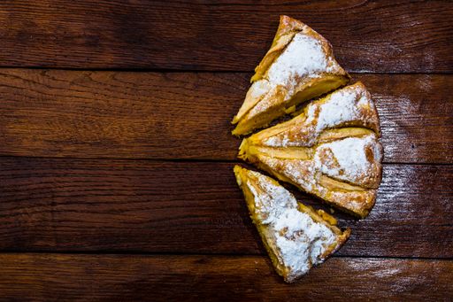 A closeup shot of a sliced apple pie with cinnamon on a rustic wooden background; cooking concept