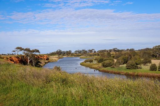 A natural view of a calm river flowing downstream in the countryside under a clear blue sky