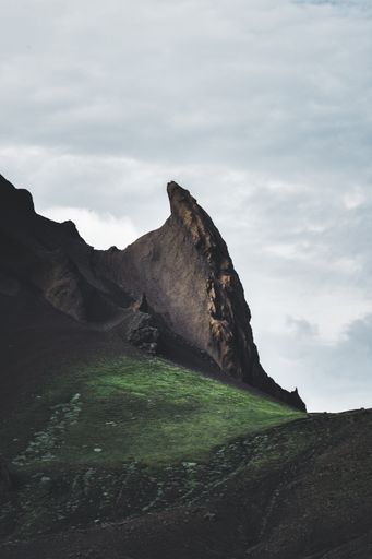 A mesmerizing vertical shot of a rocky mountain and green field under a cloudy sky