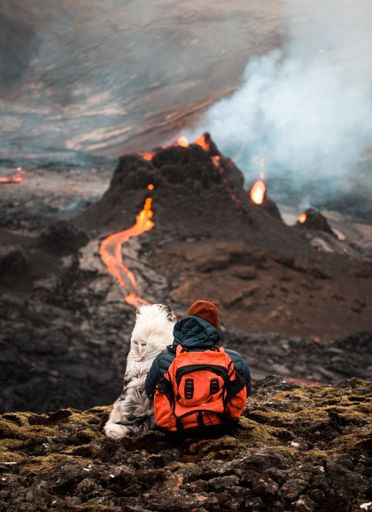 A vertical shot of a person with a dog looking at an active volcano with flowing lava