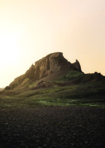 A mesmerizing vertical shot of a rocky mountain and green field under a clear sky at sunset