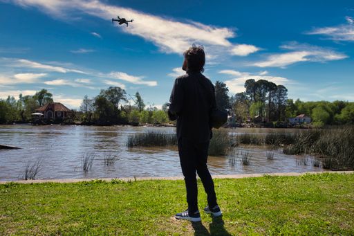 Young man flying a drone on the river bank The young man looks at the drone while he flies it without losing sight of it.