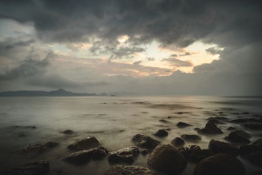 A low angle shot of the rocky shore by the sea under the beautiful cloudy sky