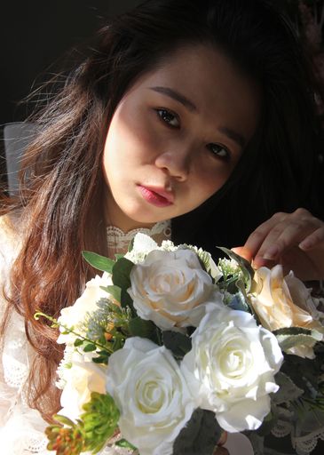 A vertical shot of a young beautiful cute elegant Southeast Asian bride holding a bouquet of roses
