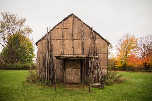An old wooden barn surrounded by trees in a field under a cloudy sky at daytime