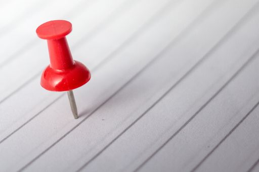A closeup of a redpushpin on a white sheet of paper with a blurry background