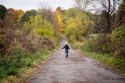 A child running through a pathway surrounded by greenery under a cloudy sky at daytime