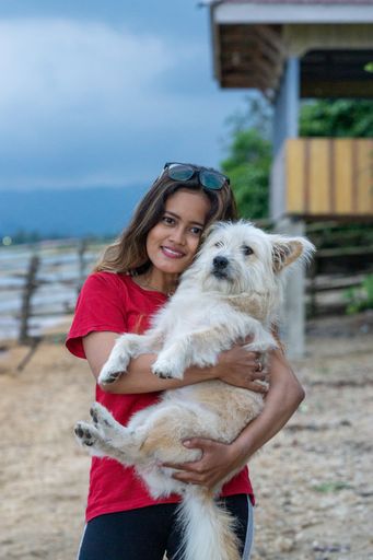 A vertical shot of an Indonesian woman hugging a dog on the shore in Togian Island