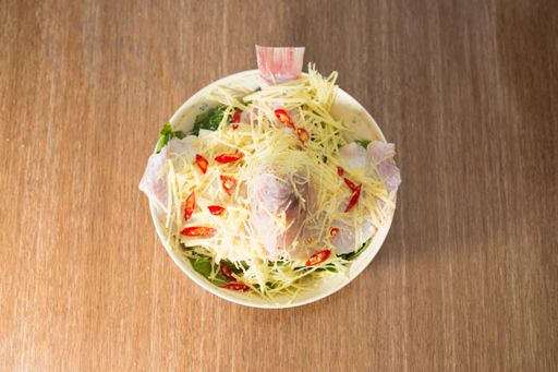 A top view of a bowl of salad with steamed tilapia fish, cheese, and vegetables on a wooden table
