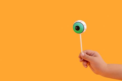 A human doll eyeball as a lollipop in the orange background with copy space; Halloween concept
