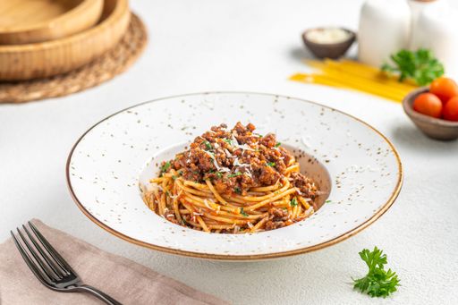 A delicious plate of spaghetti bolognese garnished with parsley, served on a rustic table setting with ingredients in the background.
