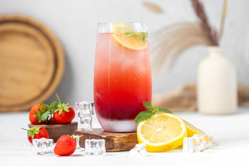 Refreshing strawberry lemonade with ice cubes, fresh strawberries, and lemon slices on a wooden table.