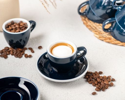 Freshly brewed coffee with scattered beans and blue cups on a light surface