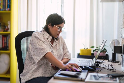 A young woman working on her computer at the desk in her room