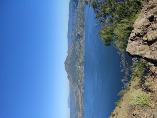 A natural view of calm sea and mountain landscape seen from a cliff under a clear blue sky
