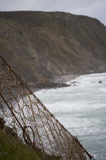 A vertical shot of a line of net next to the cliff of the beach
