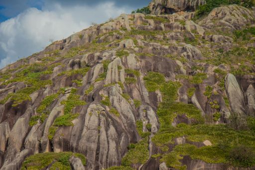 A rugged rocky hillside covered with patches of green vegetation under a partly cloudy sky.