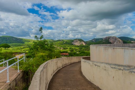 A winding path with lush greenery and rocky hills under a partly cloudy sky in a rural landscape.