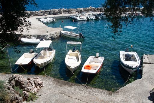 A secluded small harbor with small motorboats moored at a jetty; Nissaki village, Corfu island, Greece