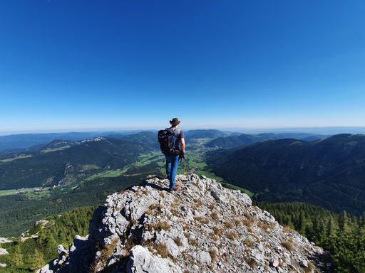 A back view of a hiker standing on the top of a rock overlooking the beautiful landscape at sunrise