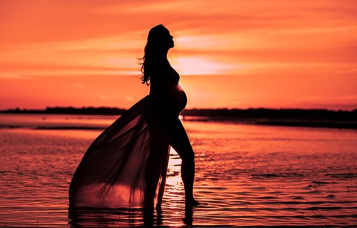 A shot of a pregnant woman silhouette posing at the sea with sunset on the sea at golden hour