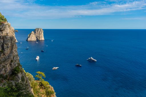Scenic view of yachts on the blue sea near Capri, Italy, with rocky cliffs and clear skies.