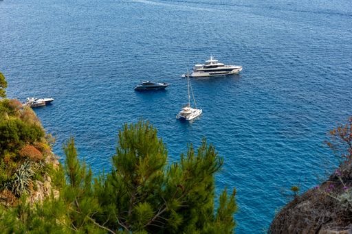 Scenic view of yachts anchored in clear blue waters near a rocky coastline with lush greenery.