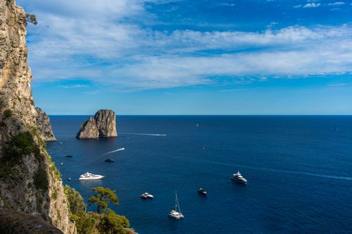 Scenic view of Capri's coastline with yachts in the blue sea and rocky cliffs under a clear sky.