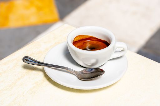 A close-up of a freshly brewed espresso in a white cup with a spoon on a saucer.