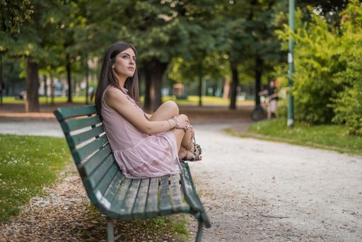 beautiful brunette girl waits alone sitting on a bench in a city park in Milan