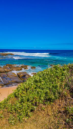 Beautiful view of the wavy sea hitting the rocky beach under the blue sky