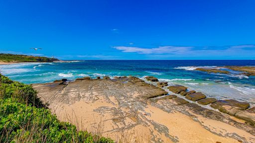 Beautiful view of the wavy sea hitting the rocky beach under the blue sky